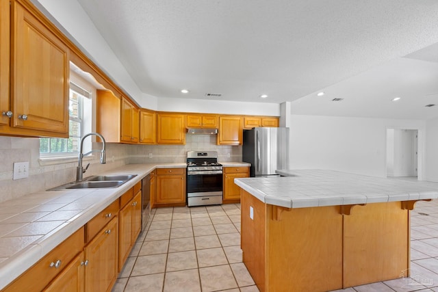 kitchen with tile counters, sink, a breakfast bar area, and appliances with stainless steel finishes