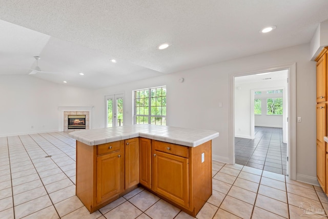 kitchen with tile counters, a kitchen island, lofted ceiling, a fireplace, and light tile patterned floors