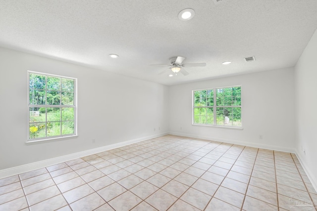 tiled empty room with ceiling fan, a textured ceiling, and a wealth of natural light