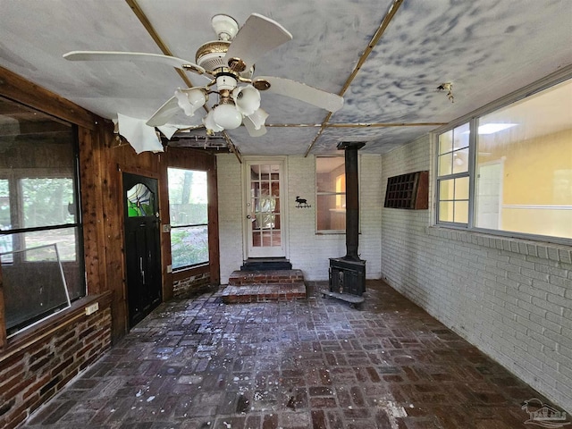 interior space featuring a wood stove, ceiling fan, and brick wall