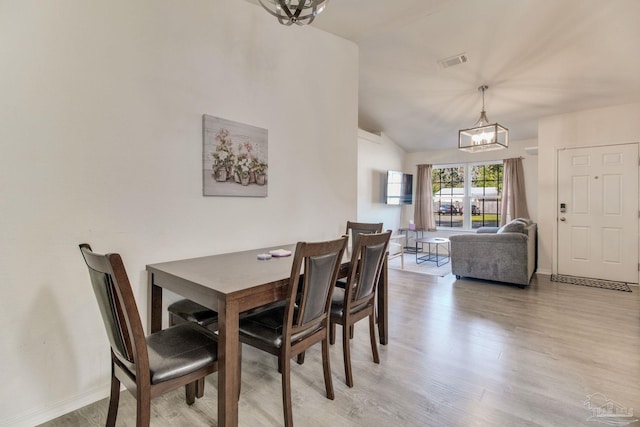 dining space with a chandelier, lofted ceiling, visible vents, baseboards, and light wood finished floors