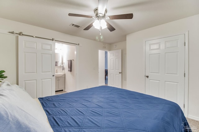 bedroom featuring visible vents, ensuite bathroom, a barn door, ceiling fan, and a sink