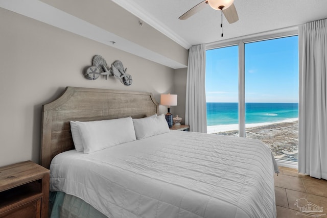 tiled bedroom featuring ceiling fan, a beach view, access to outside, a water view, and ornamental molding