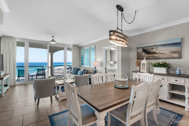 tiled dining area featuring a textured ceiling, ceiling fan with notable chandelier, crown molding, a water view, and a beach view