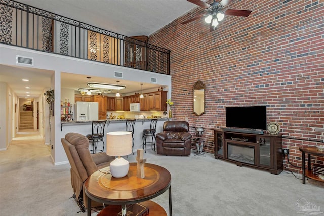 carpeted living room with a high ceiling, brick wall, and ceiling fan