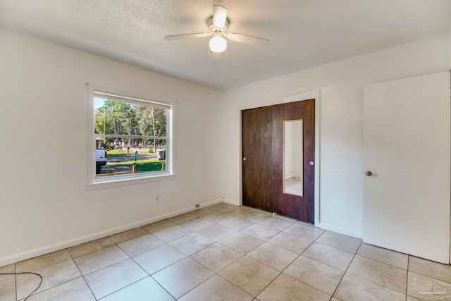 empty room with light tile patterned floors, baseboards, a textured ceiling, and a ceiling fan