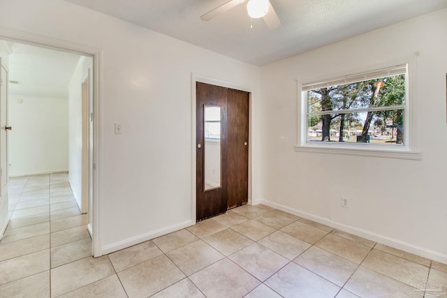 empty room featuring light tile patterned floors, baseboards, and a ceiling fan