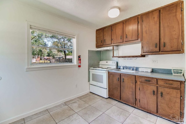 kitchen with under cabinet range hood, light tile patterned floors, brown cabinetry, electric range, and a sink