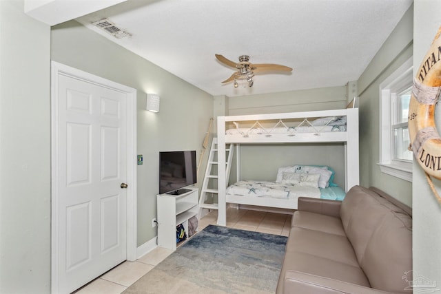 bedroom featuring ceiling fan, light tile patterned floors, and a textured ceiling