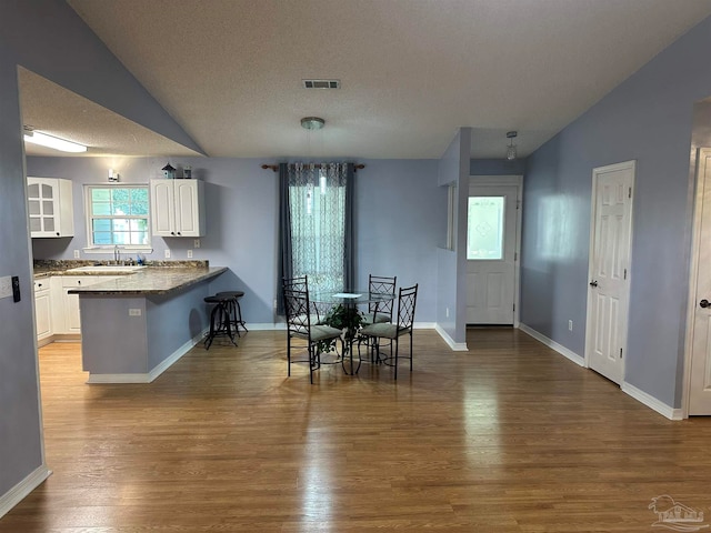 dining room with a textured ceiling, lofted ceiling, sink, and light hardwood / wood-style floors