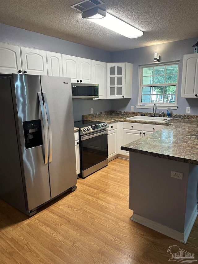 kitchen featuring a textured ceiling, light hardwood / wood-style floors, white cabinetry, and stainless steel appliances