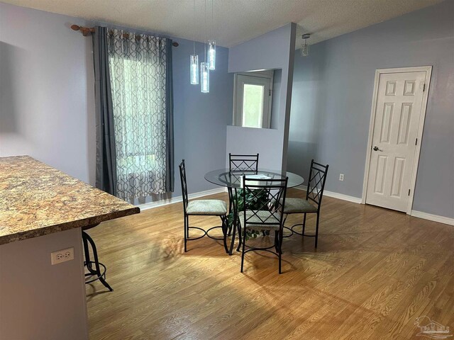 dining area with hardwood / wood-style flooring, lofted ceiling, and a textured ceiling