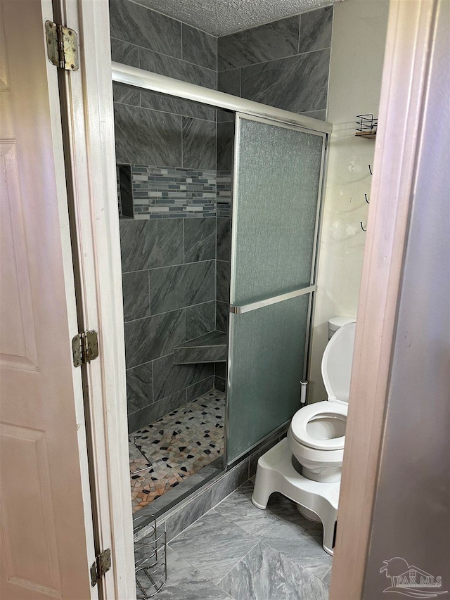 bathroom with a textured ceiling, toilet, and a shower with shower door