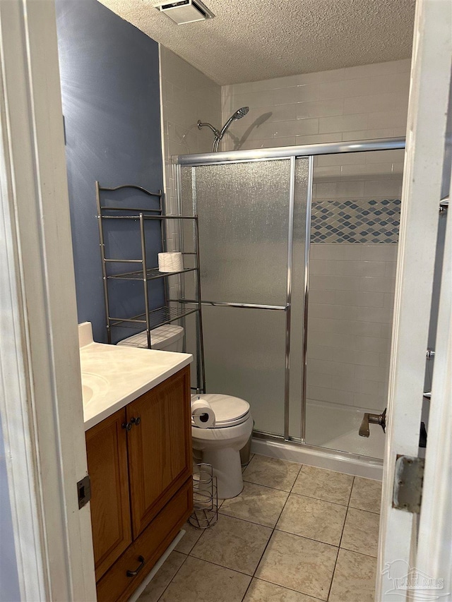 bathroom featuring a shower with shower door, vanity, a textured ceiling, toilet, and tile patterned floors