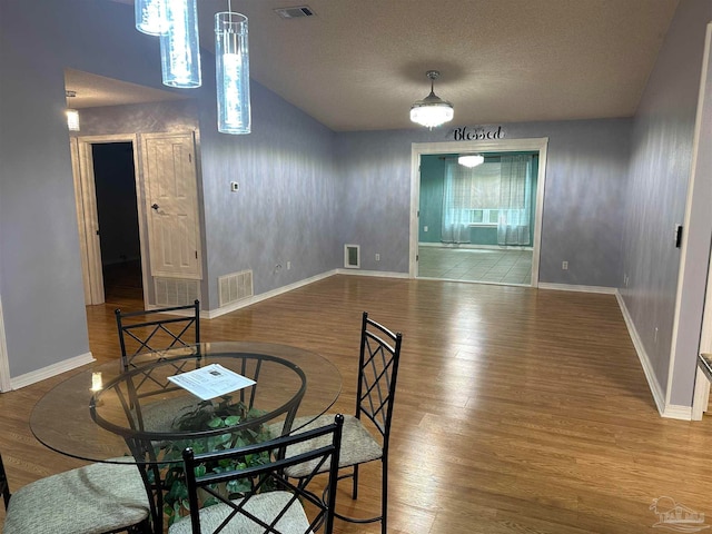 dining space with a textured ceiling, wood-type flooring, and lofted ceiling