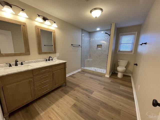 bathroom with a tile shower, vanity, wood-type flooring, and toilet