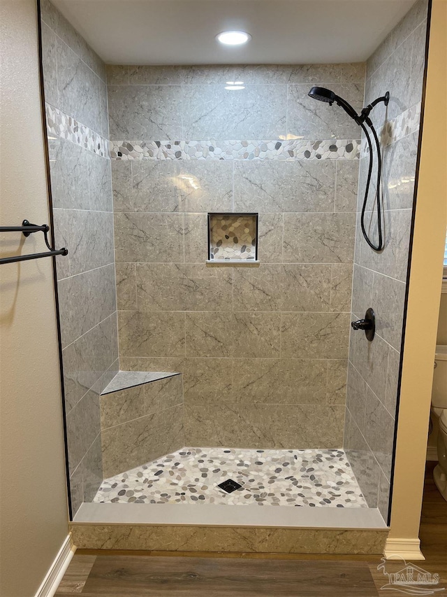 bathroom featuring wood-type flooring, tiled shower, and toilet