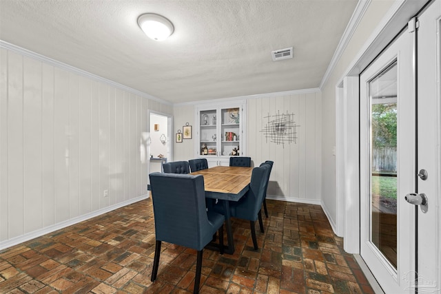 dining room featuring ornamental molding, a textured ceiling, and wooden walls