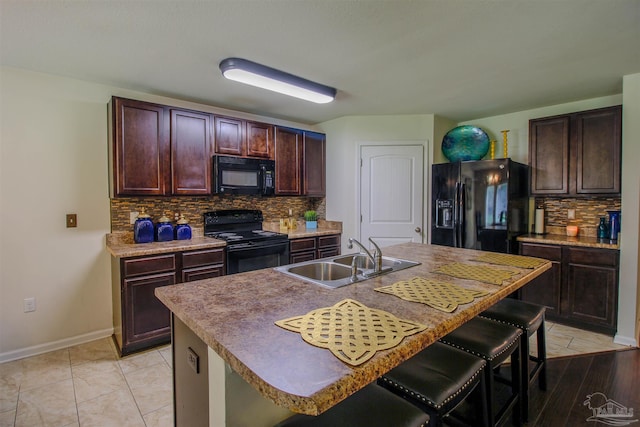 kitchen with a breakfast bar, black appliances, sink, and a center island with sink