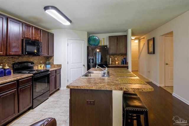 kitchen with black appliances, sink, a kitchen bar, an island with sink, and decorative backsplash