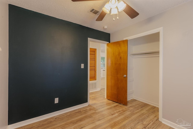 unfurnished bedroom featuring a textured ceiling, a closet, light hardwood / wood-style flooring, and ceiling fan