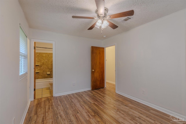 unfurnished bedroom featuring a textured ceiling, ceiling fan, ensuite bathroom, and light hardwood / wood-style flooring