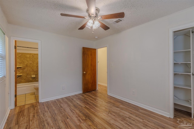 unfurnished bedroom with connected bathroom, a walk in closet, ceiling fan, and light wood-type flooring