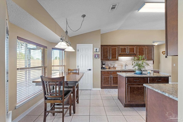 kitchen featuring decorative backsplash, light stone counters, light tile patterned floors, decorative light fixtures, and lofted ceiling