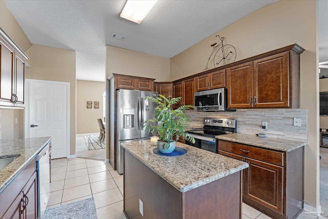 kitchen featuring light stone counters, a center island, light tile patterned flooring, and appliances with stainless steel finishes