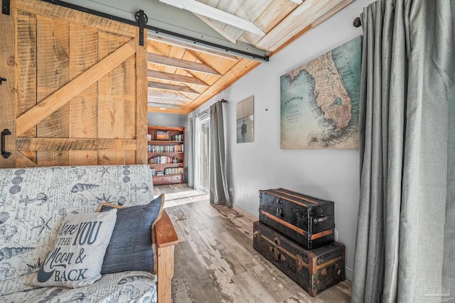 living area featuring vaulted ceiling with beams, a barn door, wood finished floors, wood ceiling, and baseboards