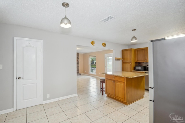 kitchen with stainless steel fridge, light stone counters, pendant lighting, a center island, and light tile patterned flooring