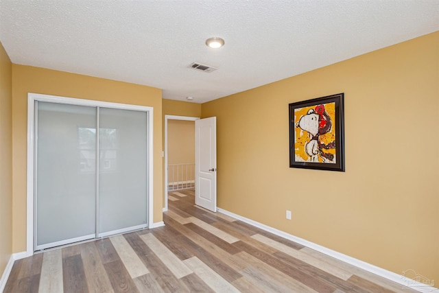 unfurnished bedroom with a textured ceiling, light wood-type flooring, and a closet