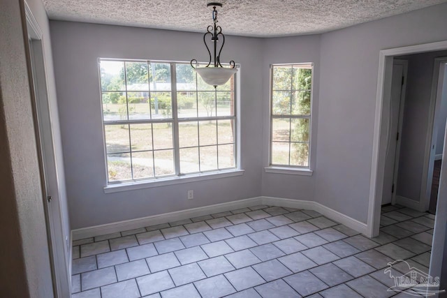 unfurnished dining area with a textured ceiling, baseboards, and tile patterned flooring