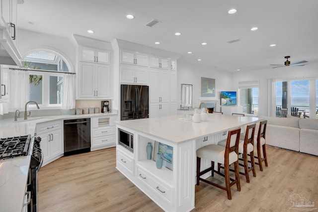 kitchen featuring black appliances, open floor plan, recessed lighting, white cabinets, and a breakfast bar area