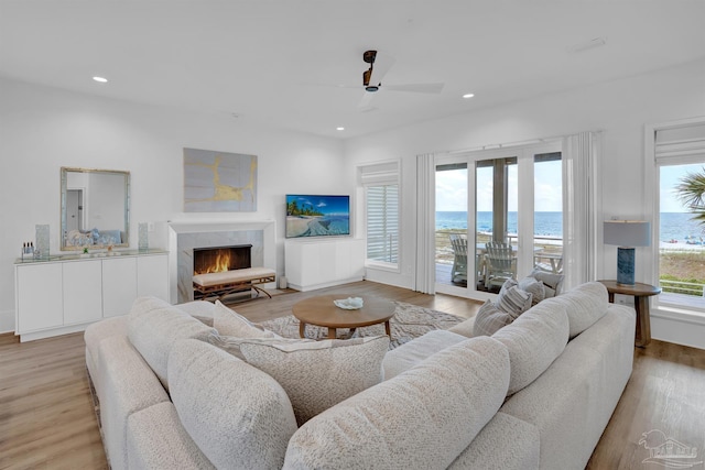 living room featuring ceiling fan, a premium fireplace, recessed lighting, light wood-type flooring, and baseboards