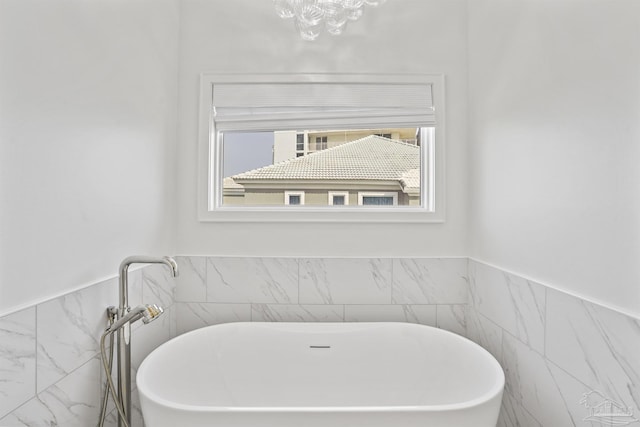 full bathroom with a chandelier, a freestanding tub, and tile walls