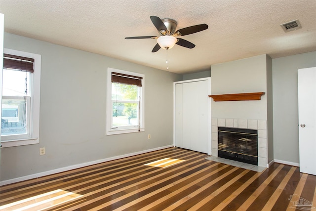 unfurnished living room with a textured ceiling, a ceiling fan, visible vents, wood finished floors, and a tiled fireplace