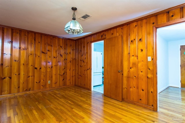 empty room with light wood-style floors, wooden walls, baseboards, and visible vents