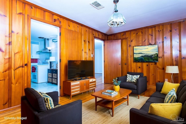 living room featuring light wood-style flooring, a chandelier, wooden walls, and visible vents