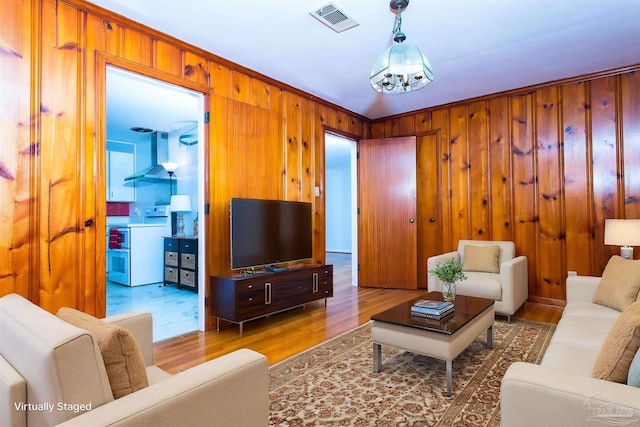 living room with wood walls, visible vents, an inviting chandelier, and wood finished floors