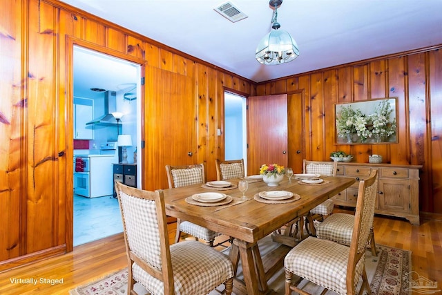 dining room featuring light wood-style floors, wooden walls, visible vents, and an inviting chandelier