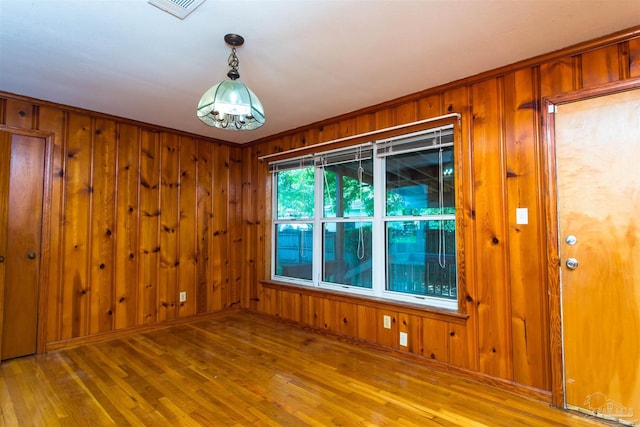 empty room featuring wood finished floors, wooden walls, and visible vents