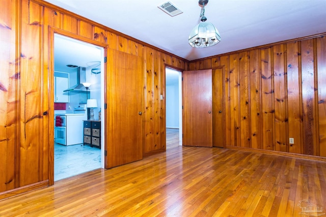 empty room featuring wooden walls, visible vents, light wood finished floors, and a chandelier