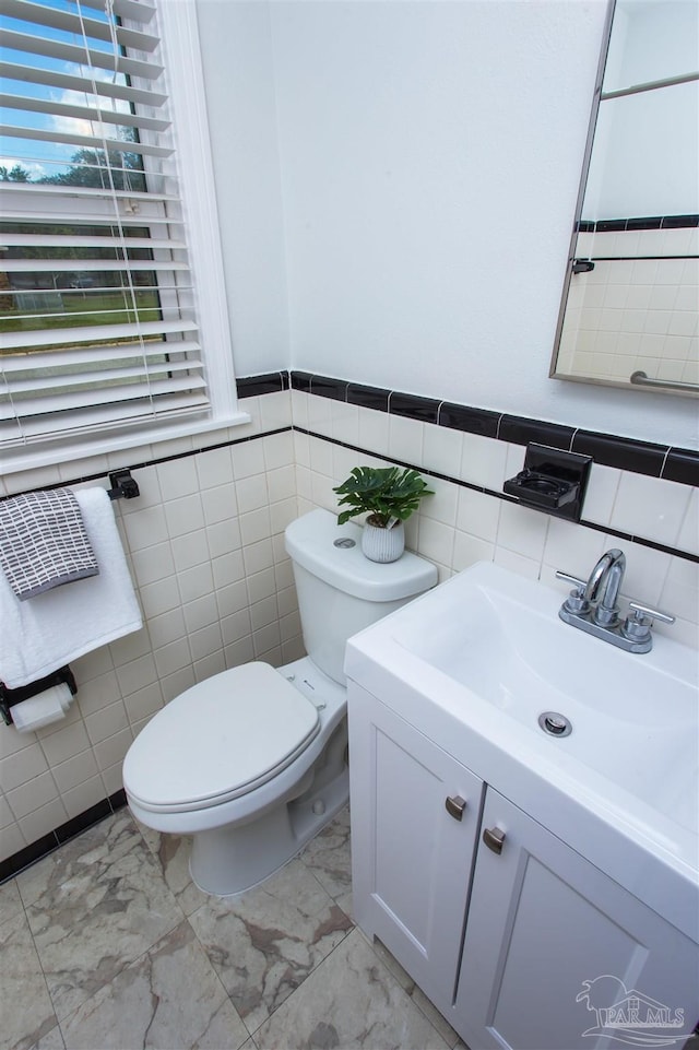 bathroom with tile walls, toilet, vanity, a wainscoted wall, and marble finish floor