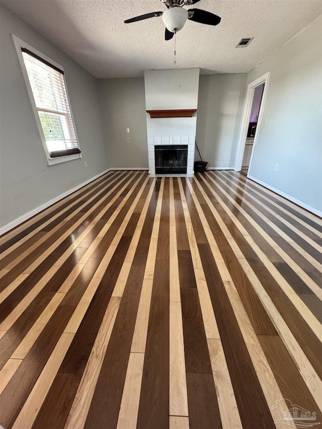unfurnished living room with visible vents, a tiled fireplace, a ceiling fan, a textured ceiling, and wood finished floors