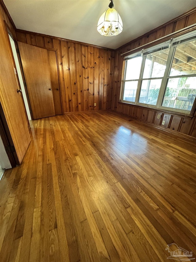 spare room featuring wood walls, a notable chandelier, and hardwood / wood-style flooring