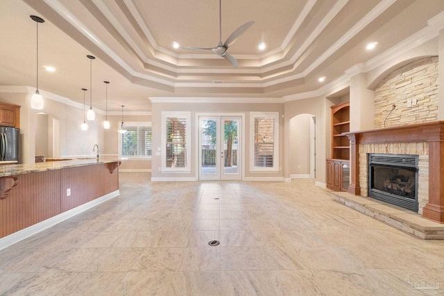 unfurnished living room featuring built in features, ceiling fan, a tray ceiling, crown molding, and a fireplace