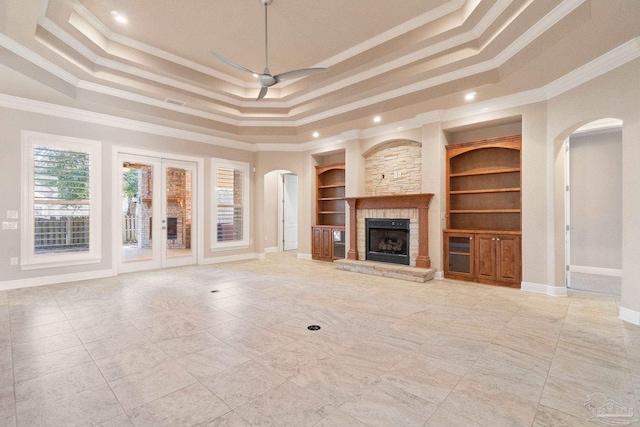 unfurnished living room with built in shelves, a tray ceiling, and crown molding