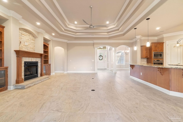 unfurnished living room featuring arched walkways, ceiling fan, a stone fireplace, and ornamental molding