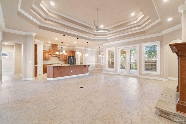 unfurnished living room with arched walkways, ceiling fan, a raised ceiling, and baseboards